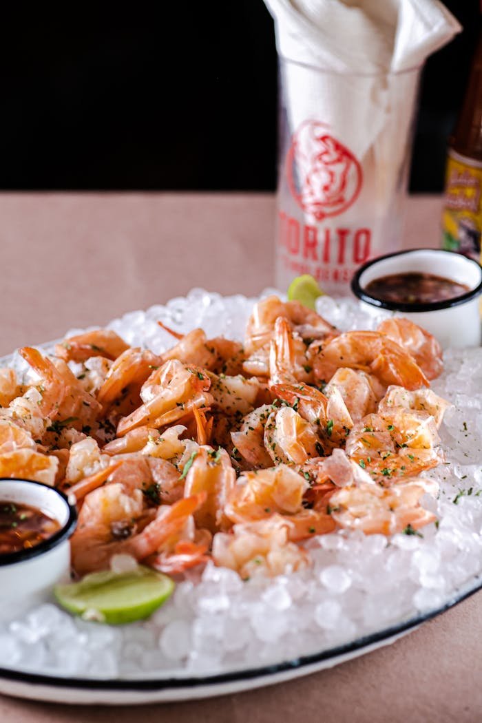 gallery-5 Delectable shrimp served on ice with dipping sauces, garnished with herbs and lime.