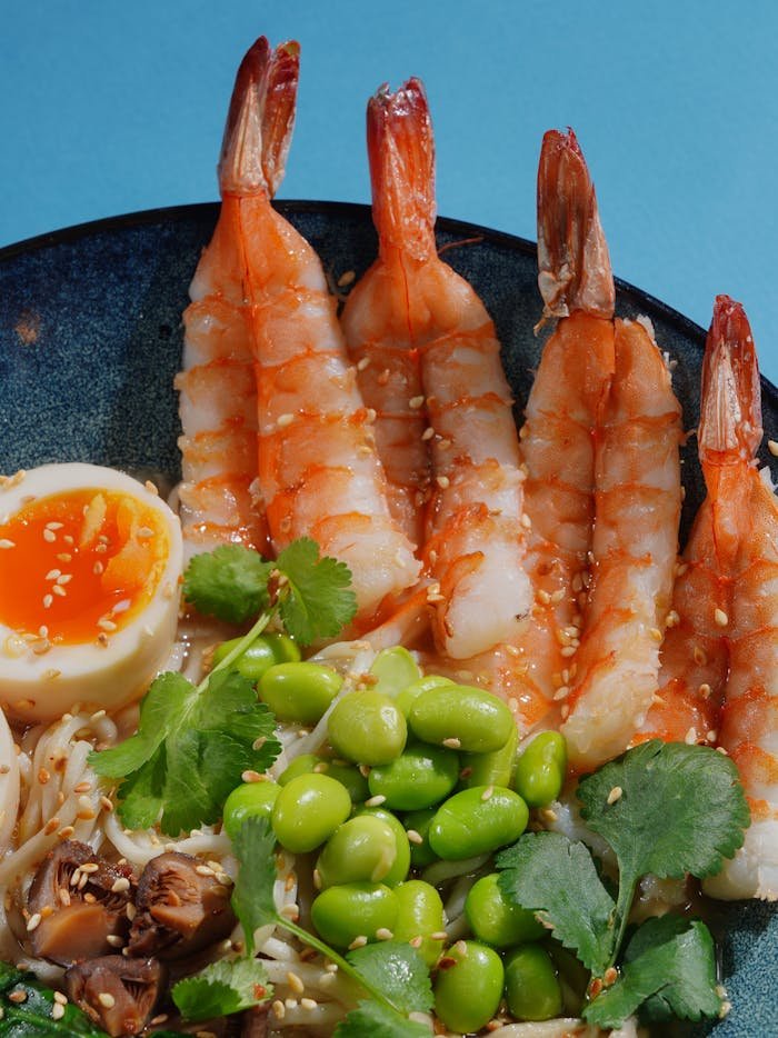 Close-up of a vibrant shrimp and vegetable noodle bowl on a blue background.