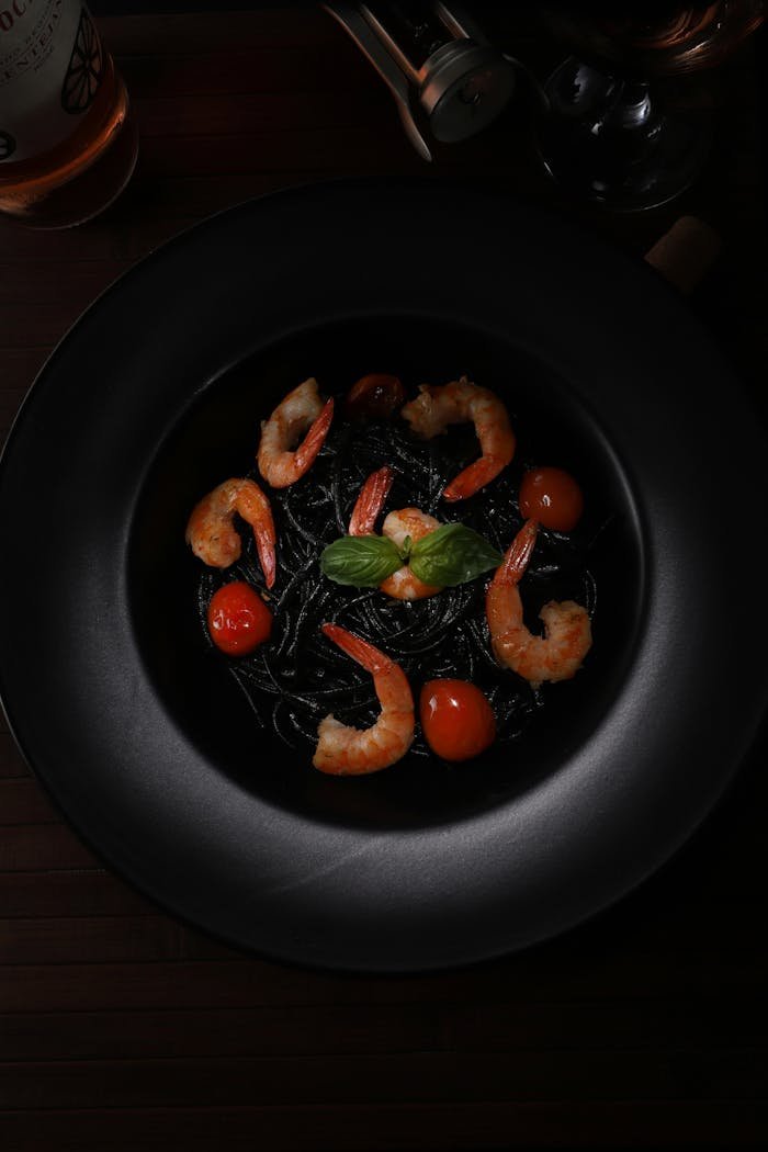 Elegant food photography featuring shrimp and squid ink pasta on a dark plate, top view.