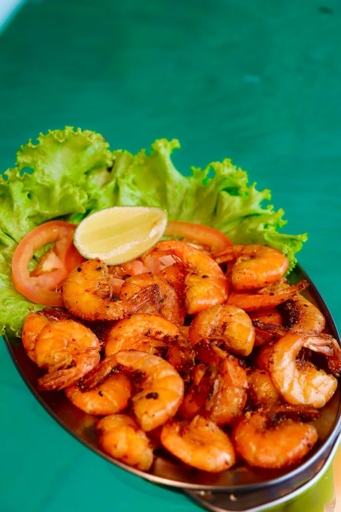 services-02 Close-up of a grilled shrimp platter garnished with lemon, lettuce, and tomatoes on a vibrant green background.