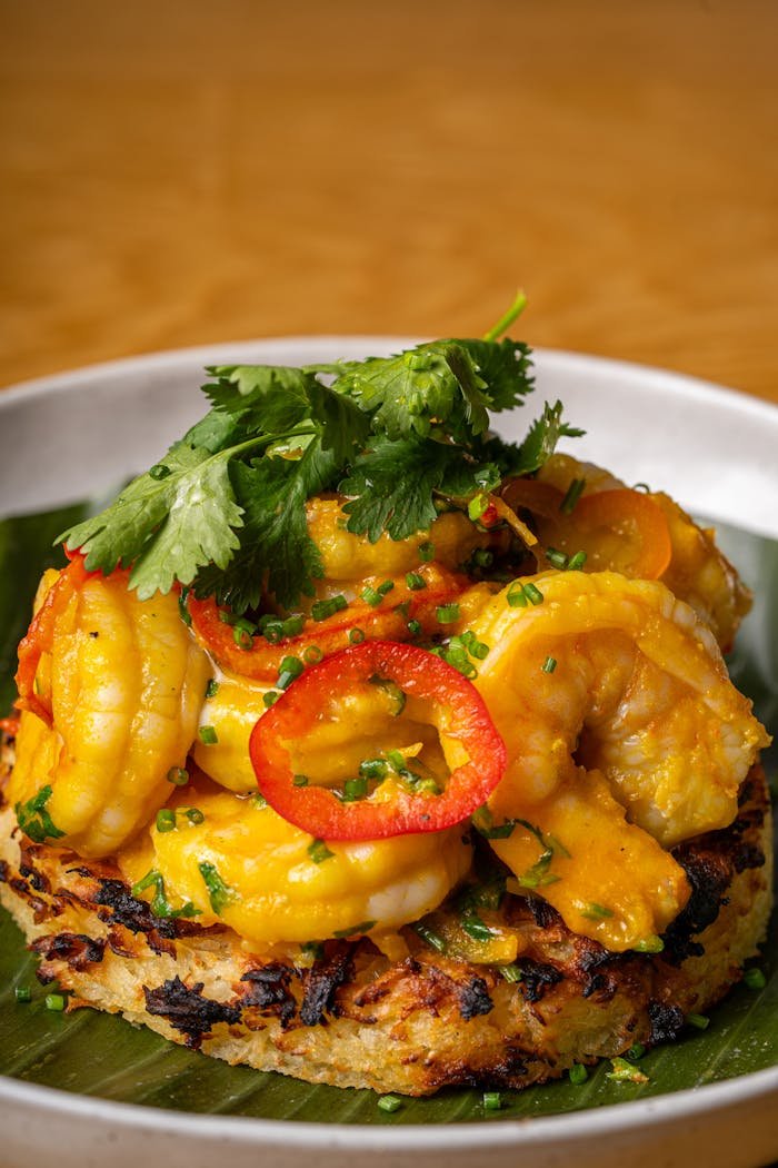 Close-up of a grilled shrimp dish with cilantro and red pepper garnished on a white plate.