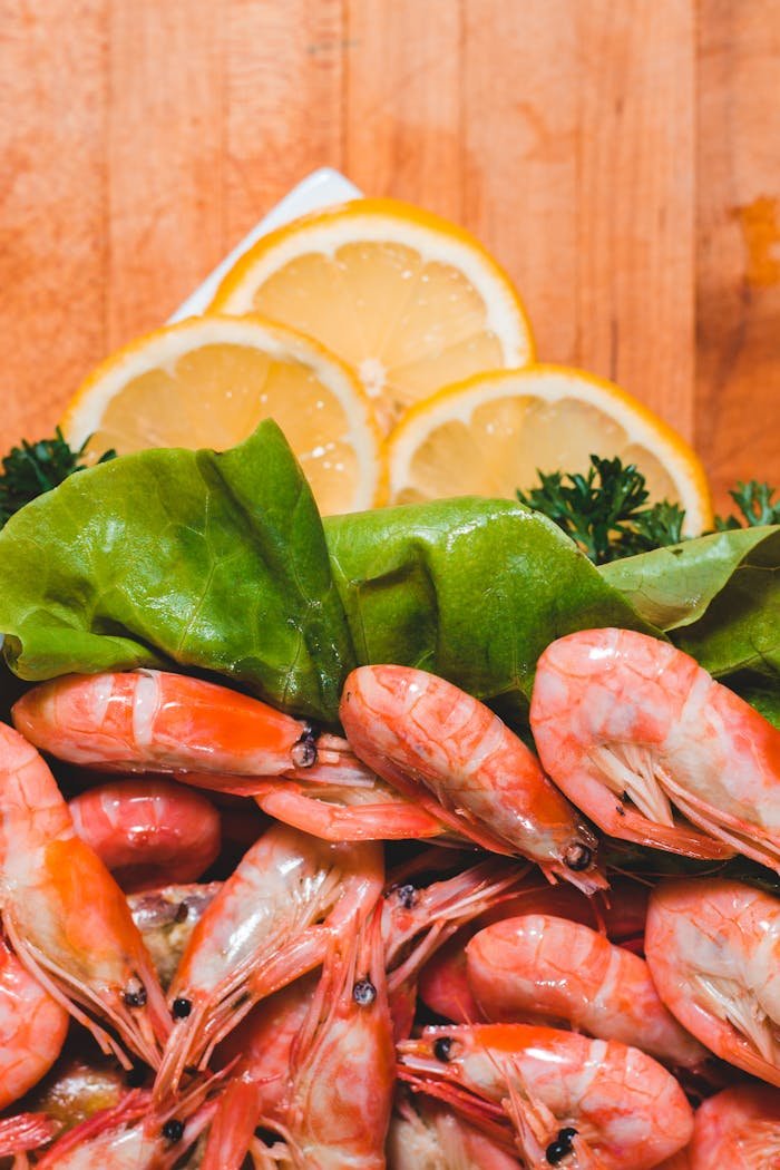 Delicious shrimp served with lemon slices and fresh greens on a wooden table.