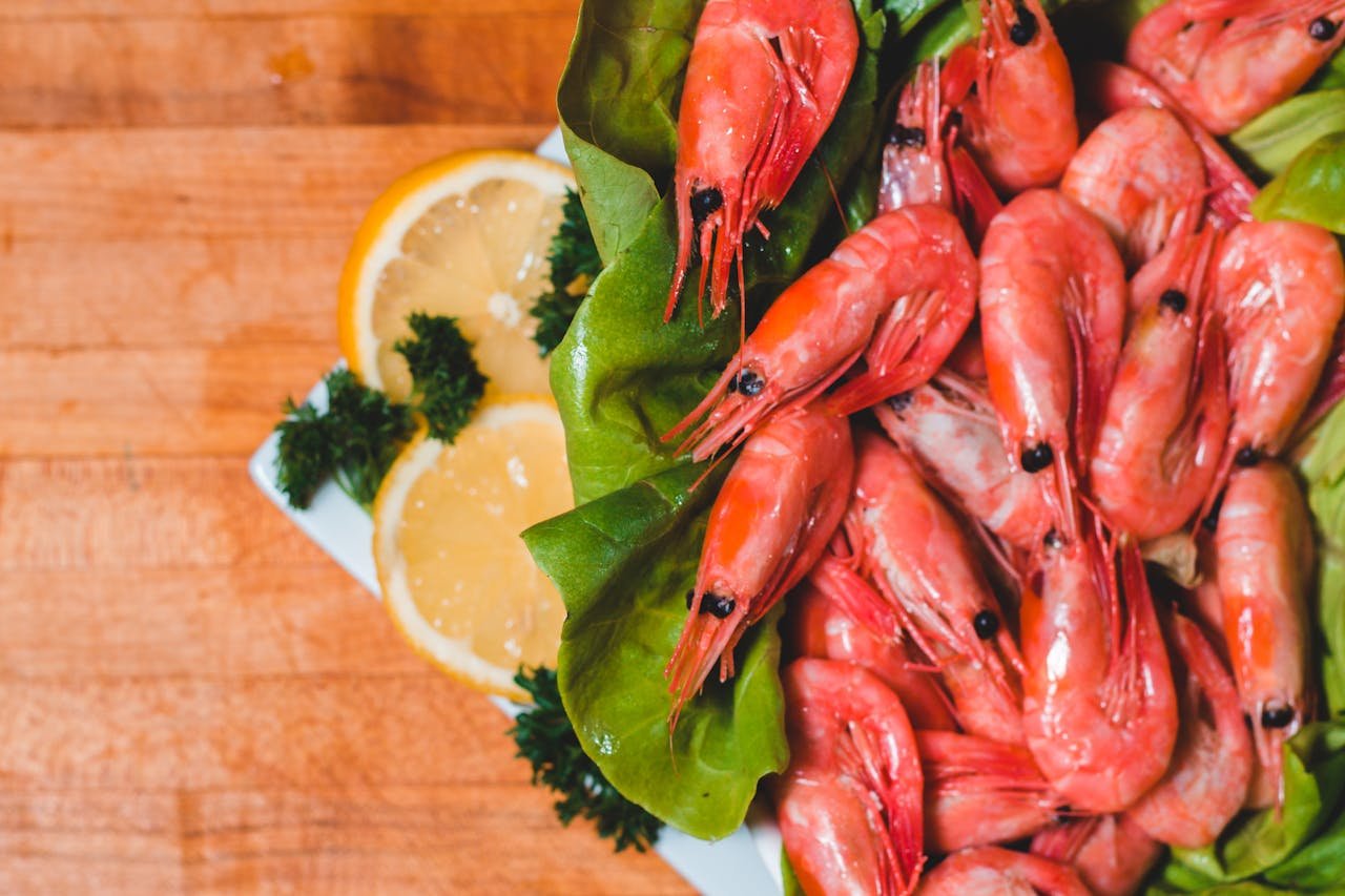 services-03 Vibrant seafood platter with shrimp, lemons, and herbs on a wooden surface.